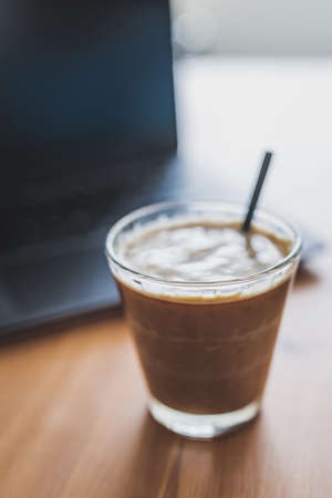 soy latte in a clear mug next to laptop on dining table, concept of remote working or coffee break at the officeの写真素材