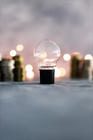 idea light bulb with stacks of different golden and silver coins representing a big amount of money shot on grey concrete background with fairy light, success and abundance conceptの写真素材