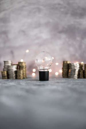 idea light bulb with stacks of different golden and silver coins representing a big amount of money shot on grey concrete background with fairy light, success and abundance conceptの写真素材