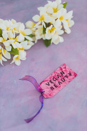 cruelty free beauty products concept, Vegan Beauty message on label over purple background with white tropical frangipani flowers in the backgroundの写真素材
