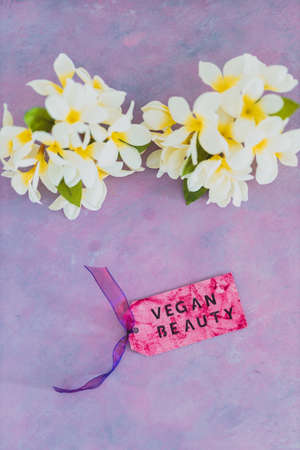 cruelty free beauty products concept, Vegan Beauty message on label over purple background with white tropical frangipani flowers in the backgroundの写真素材