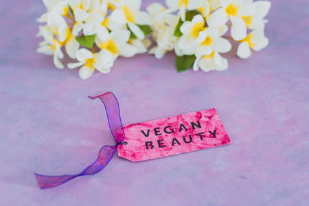 cruelty free beauty products concept, Vegan Beauty message on label over purple background with white tropical frangipani flowers in the backgroundの写真素材