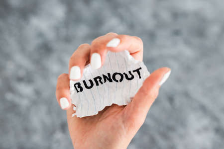 hand holding Burnout text on scrunched up piece of paper, psychology or mental health conceptの写真素材