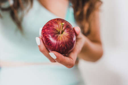 fit young woman holding red apple towards the camera shot at shallow depth of field, concept of healthy nutrition and weight lossの写真素材