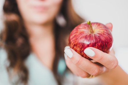 fit young woman holding red apple towards the camera shot at shallow depth of field, concept of...