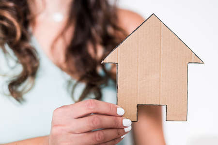 real estate and first time home buyers concept, woman holding cardboard house icon towards the cameraの写真素材