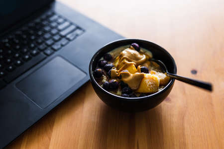 eating mango blueberries oatmeal while working from home on a laptop, concept of remote working or lunch at the officeの写真素材