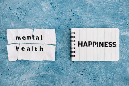 Happiness text on notepad next to Mental health text on torn sticky taped page, psychology and...