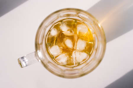 golden brown or amber liquor in stein glass with ice on white background with harsh sunlight shot from top down perspectiveの写真素材