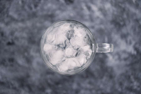 pint glass with tap water and ice cubes over grey concrete background, concept of drinking enough...