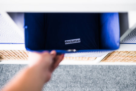 hand grabbing storage cube with Declutter label inside of it with unfocused storage cabinet with...