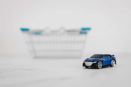 toy car inside of shopping basket over white marble background, concept of buying a new carの写真素材