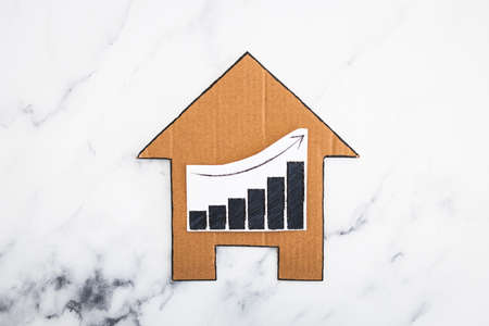 mortgages rentals and property prices increasing, house icon made of cardboard with graph showing stats going up conceptual image on marble backgroundの写真素材