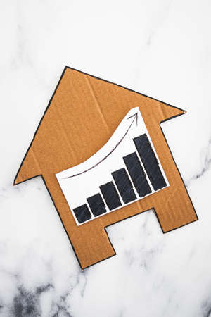 mortgages rentals and property prices increasing, house icon made of cardboard with graph showing stats going up conceptual image on marble backgroundの写真素材