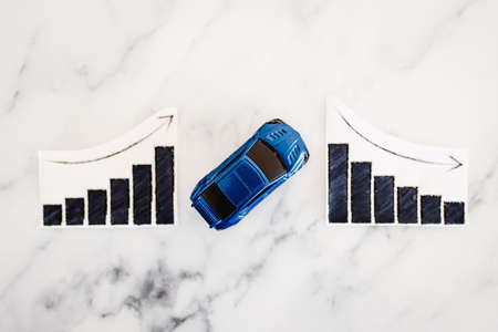 car loans rentals and car prices increasing, blue toy car next to graph showing stats going up conceptual image on marble backgroundの写真素材