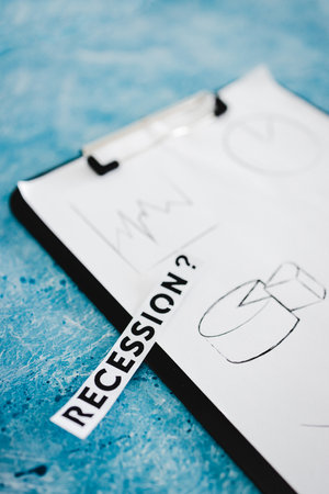 recession and stagnating economy conceptual image with text next to clipboard showing a multitude of stas and graphsの写真素材