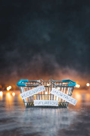 economy after conceptual image, inflation shortages and recession texts on empty shopping basket  on dark background with lightsの写真素材