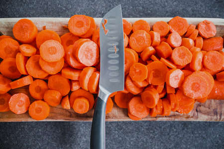 close-up of fresh carrots getting sliced on wooden chopping board with knife in the centre, concept of simple natural healthy ingredientsの写真素材