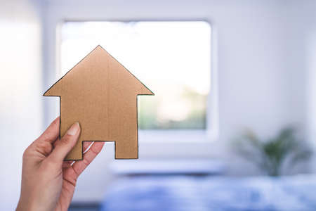 hand holding house icon in front of bedroom bokeh, concept of buying a house and real estate market or dream home or family lifeの写真素材