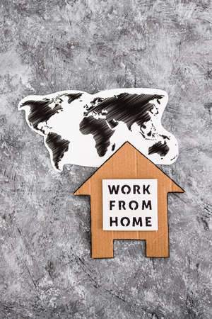 work from home sign with world map and house made of cardboard on grey background, concept of digital nomads working remotely or wfh days during lockdowns or covid-19 isolationの写真素材