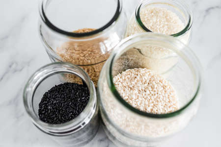 pantry jars with different types of rice including black brown arborio and sushi rice, concept of simple staple ingredientsの写真素材