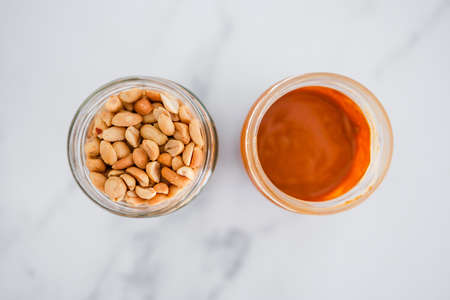 glass jars with peanuts and peanut butter on white marble background, natural healthy pantry staple ingredientsの写真素材