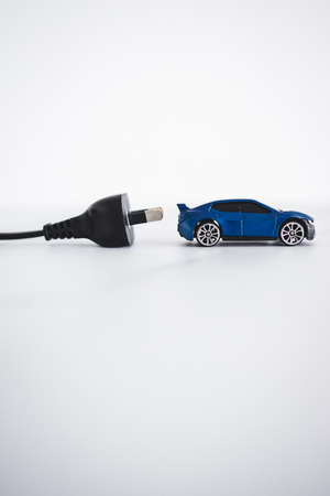concept of electric or hybrid vehicles, blue toy car with plug behing it