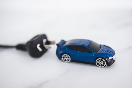 concept of electric or hybrid vehicles, blue toy car with plug behing itの写真素材