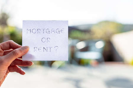 hand holding mortgage or rent sign in front of backyard bokeh, concept of real estate affordability and property marketの写真素材