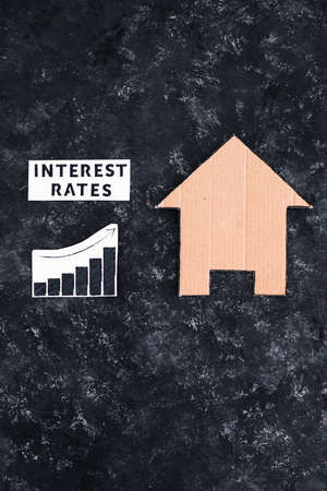interest rates text and graph showing cost of financing going up next to house made of cardboard, concept of the global economy after the covid-19 pandemicの写真素材