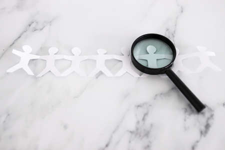 staff shortages and hiring personnel conceptual image, paper people chain with magnifying glass...