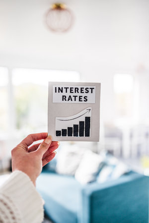 property affordability and home loan payment increases, hand holding interest rates sign with graph showing stats going up in front of living room bokehの写真素材