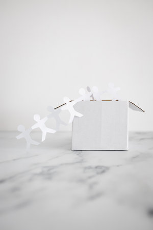 Think outside the box concept with paper people chain getting out of a white box on white...