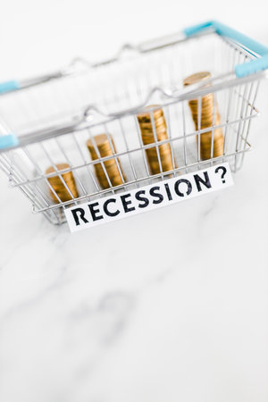 prices going up and rising inflation concept with Recession text in front of shopping basket with growing stacks of coins inside of it, global economy struggling after the covid-19 pandemicの写真素材