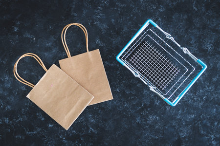 marketing promotions and customer purchasing habits conceptual still-life, shopping basket and paper bags shot from topdown perspective on dark grey backgroundの写真素材
