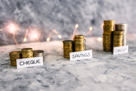 Cheque savings and credit account texts in front of growing stacks of coins. Conceptual image about...
