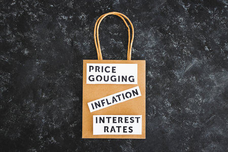 Inflation Interest Rates and Price Gouging texts on paper shopping bag on dark background, symbol of excessive pricingの写真素材