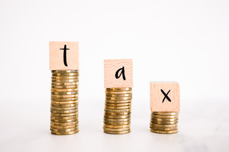 Tax text on top of decreasing stacks of coins, symbol of decreasing tax rates and feesの写真素材