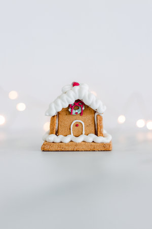 festive Christmas gingerbread house with fairy lights in the background on off white minimalist...