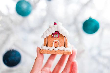 gingerbread house in front of snowy Christmas tree with white and blue tones, concept of festive season and holiday traditionsの写真素材