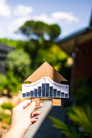 interest rates  or property prices going up then down again, house with graph and backyard bokeh in the backgroundの写真素材