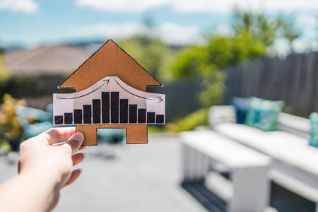 interest rates  or property prices going up then down again, house with graph and backyard bokeh in the backgroundの写真素材