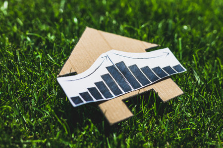 interest rates going up then down again, graph showing stats increasing and decreasing over house icon made of cardboard on green lawnの写真素材