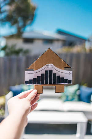interest rates  or property prices going up then down again, house with graph and backyard bokeh in the backgroundの写真素材