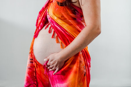 pregnant woman touching her bump in the latest stage of pregnancy, mid-section showing the belly and body shape wearing a summer sarong. no face in the frameの写真素材