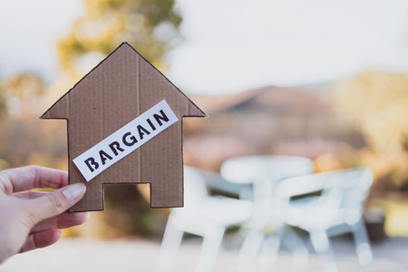 Bargain label on cardboard house in front of backyard and patio bokeh, concept of finding a dream property and real estate market affordabilityの写真素材