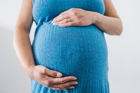 pregnant woman cudling her bump in the ninth month, mid-section showing the belly and body shape wearing blue dressの写真素材