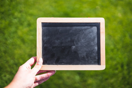 hand holding small blackboard with blank copy space in front of perfect green grass lawn, with space for your textの写真素材
