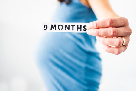 pregnant woman holding 9 Months sign towards the camera wearing blue dress in the last month of pregnancy,  shot at shallow depth of fieldの写真素材