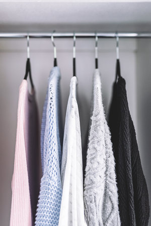 minimalist capsule wardrobe selection of womenswear sweaters and cardigans hang on wardrobe rod with matching hangers shot at shallow depth of fieldの写真素材